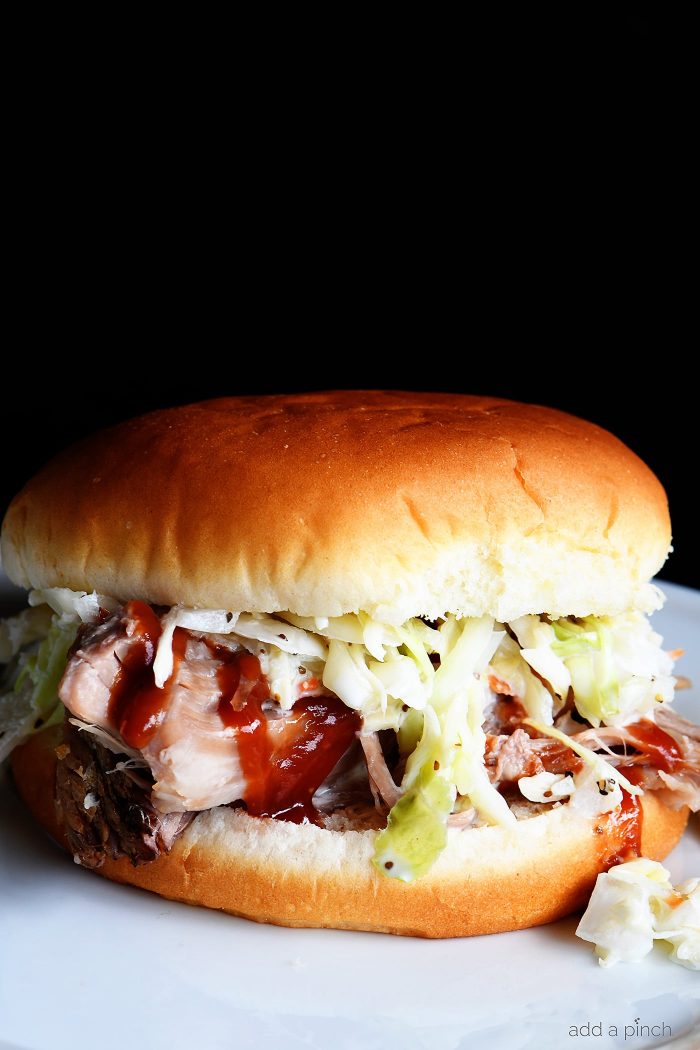 Pulled Pork Sandwich drizzled with homemade bbq sauce and topped with coleslaw on white plate // addapinch.com