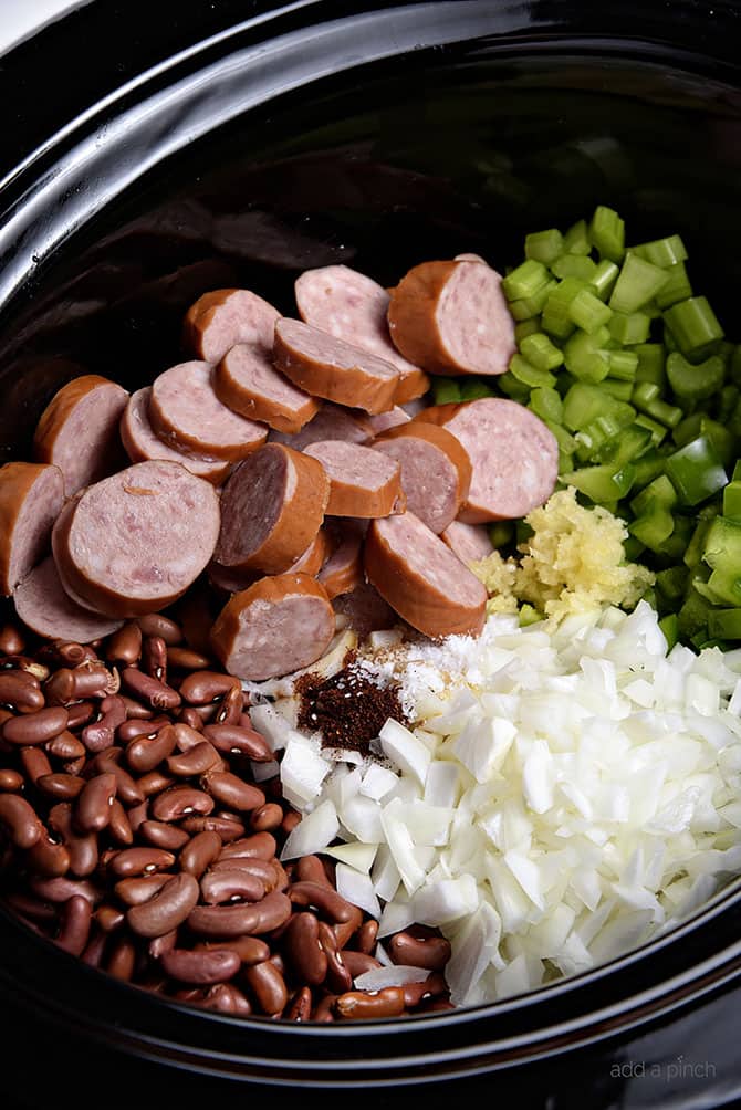 Slow Cooker insert with red beans, onions, seasonings, bell pepper, sliced sausage.