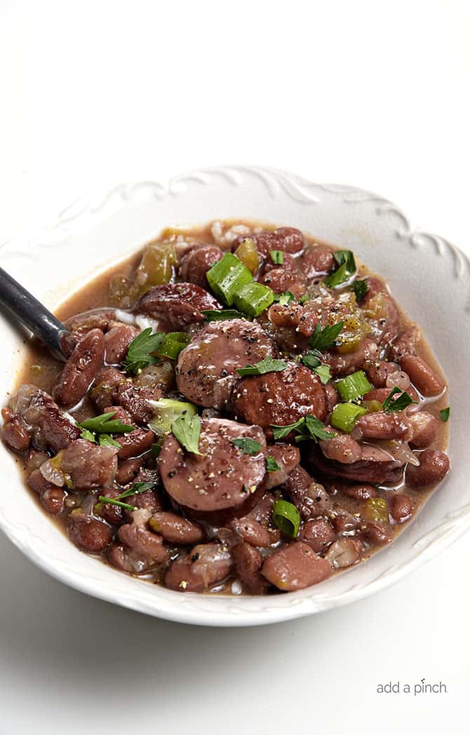 Spoon in a bowl of garnished Red Beans with sausage and bell pepper and onions // addapinch.com