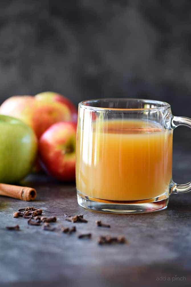 Homemade Apple Cider in glass mug surrounded by fresh apples and spices on a granite countertop.