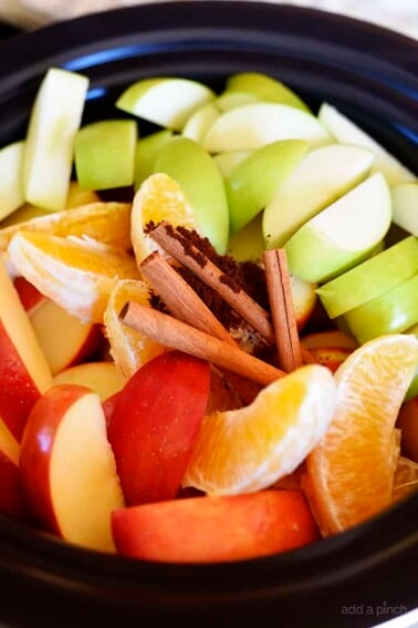 Orange and apple slices, cinnamon sticks and spices in a large crock.