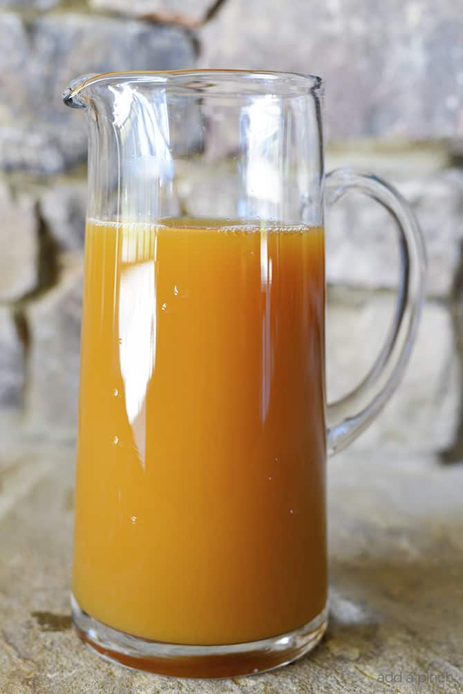 Tall glass pitcher holds fresh homemade apple cider sitting on a stone countertop.