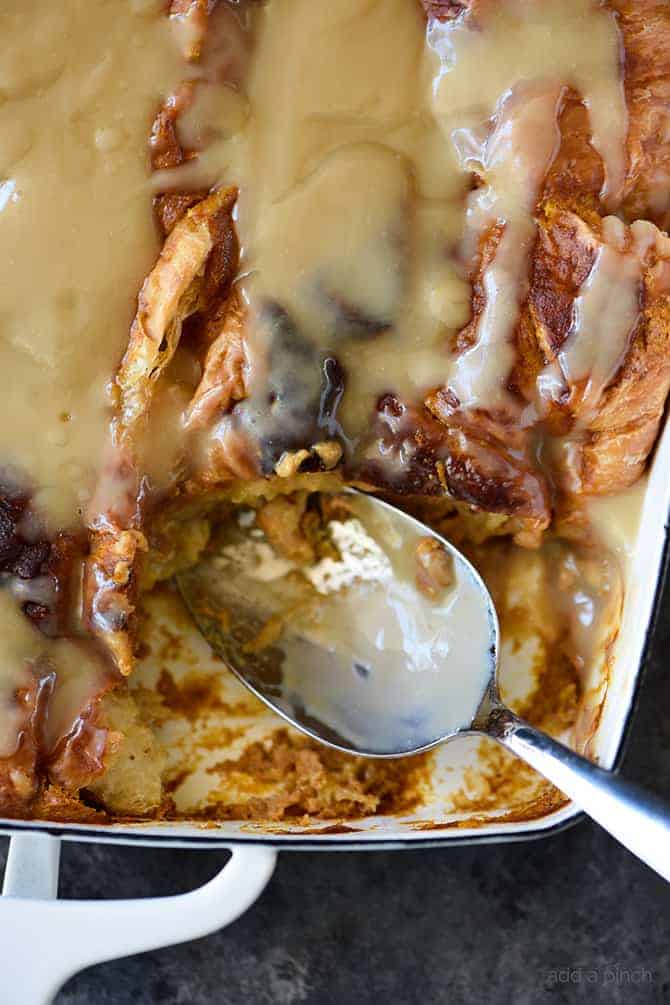 Spoon in white baking dish has scooped out serving of pumpkin bread pudding with maple cream sauce // addapinch.com