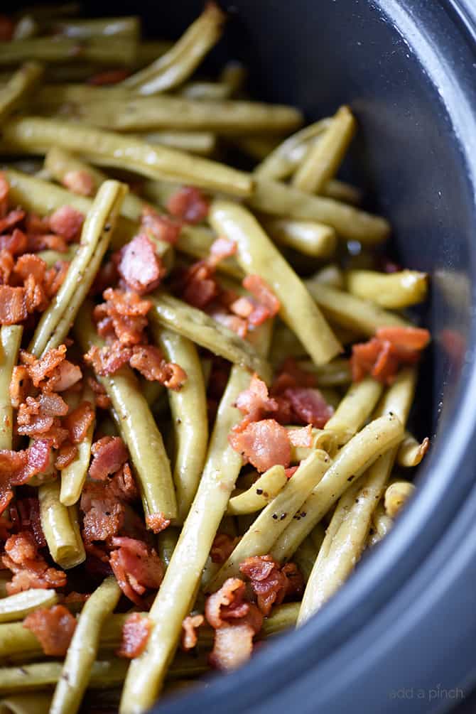 Photo of green beans topped with bacon in slow cooker.