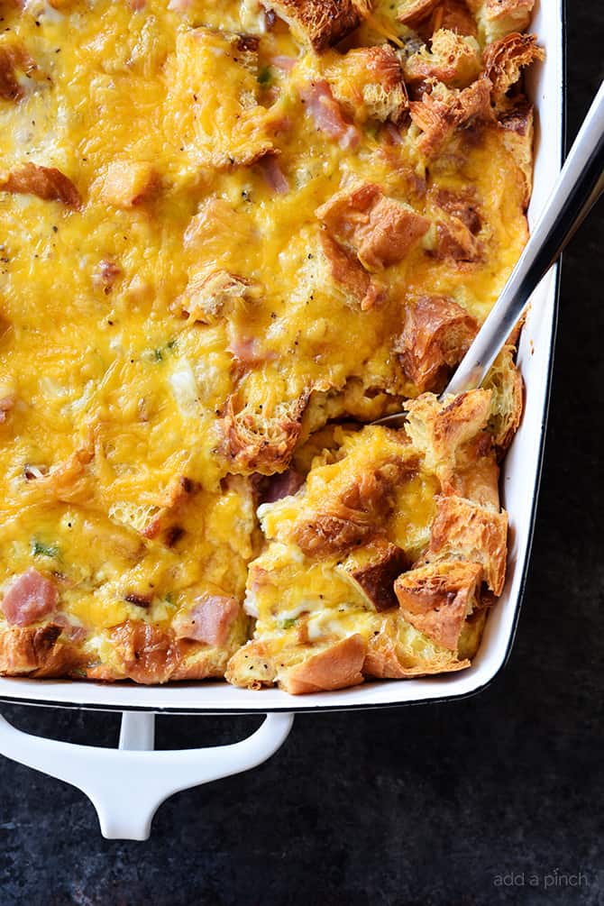 White baking dish filled with croissant breakfast casserole showing ham and melted cheeses. 