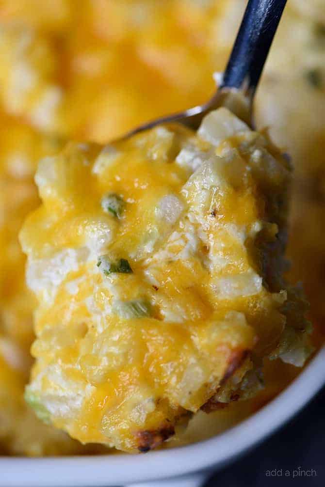 Spoon full of cheesy potato side dish in a baking dish.