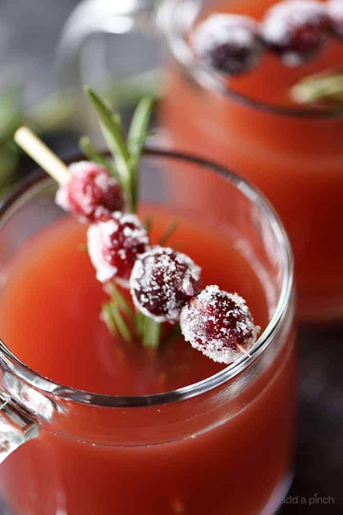 Cranberry Pomegranate Cider in glass mugs, garnished with skewer of sugared cranberries and rosemary sprig