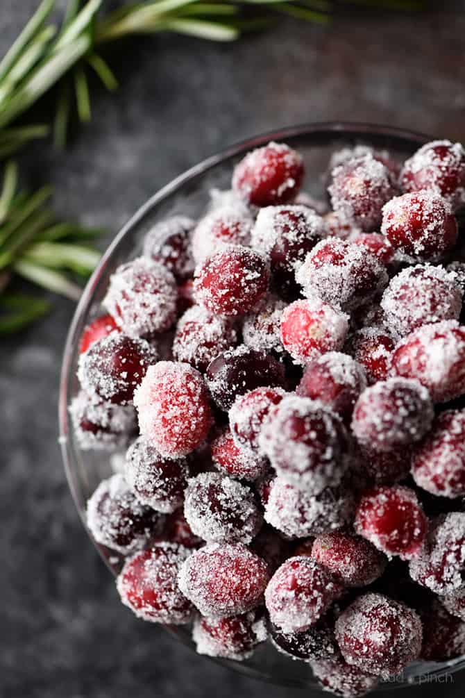 Sugared Cranberries in a serving bowl surrounded with rosemary garnish  // addapinch.com