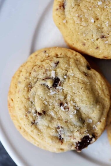 photograph of chocolate chip cookie on a white plate on a dark background.