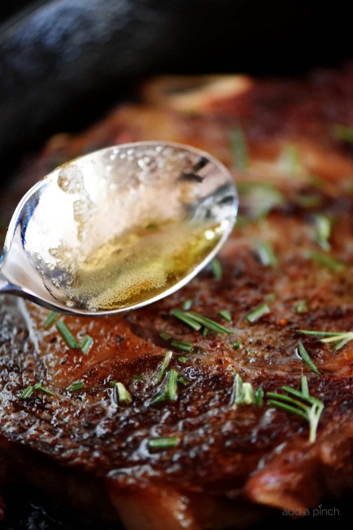 Butter-basting a steak topped with rosemary with a stainless spoon in a skillet // addapinch.com