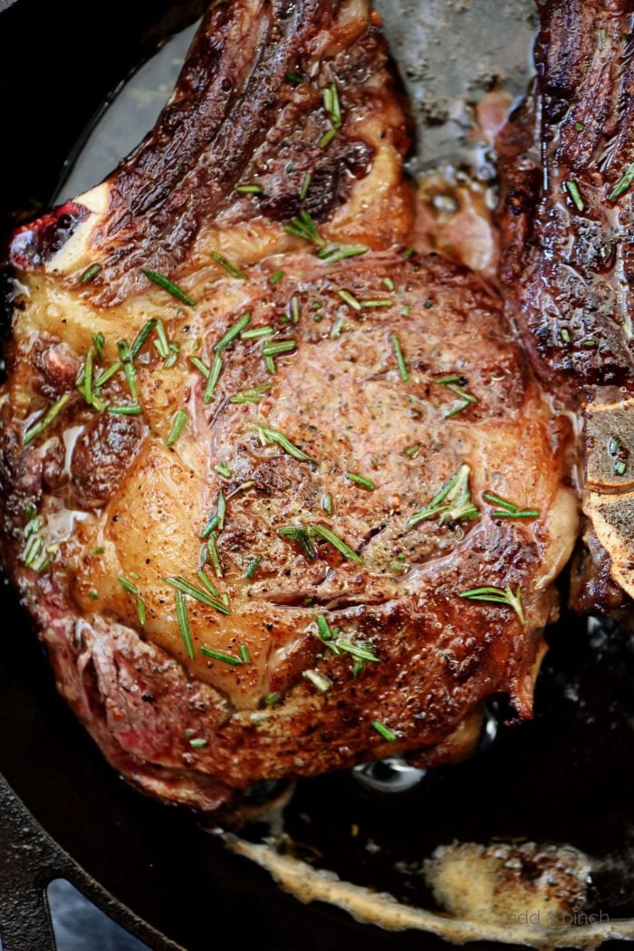 Iron skillet cooking a juicy steak in butter. Steak garnished with chopped rosemary // addapinch.com