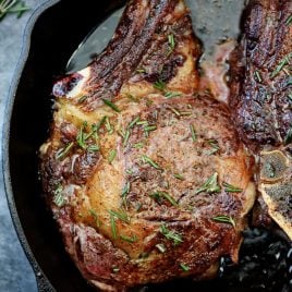 Cast iron skillet with a butter-basted ribeye steak topped with rosemary.