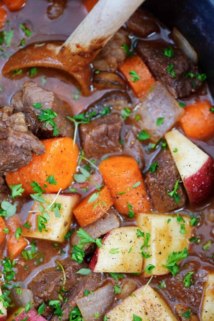 Closeup of wooden spoon stirring tender chunks of beef with carrots, onion and thyme in a rich sauce // addapinch.com