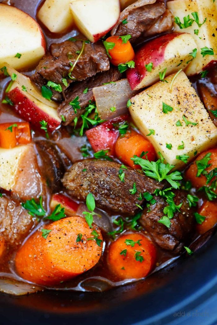 Close up photo of vegetables, beef, and a thick, rich sauce and fresh thyme.