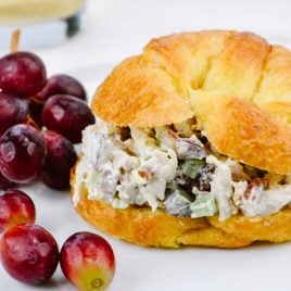 Chicken Salad on a croissant surrounded by red grapes.