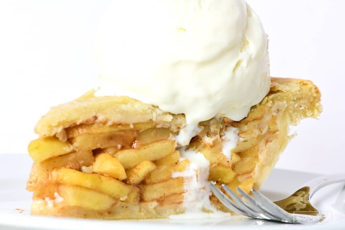 Slice of apple pie topped with vanilla ice cream on a white plate.