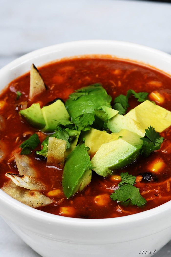 Chicken Tortilla Soup topped with cilantro and avocado in a white bowl - from addapinch.com