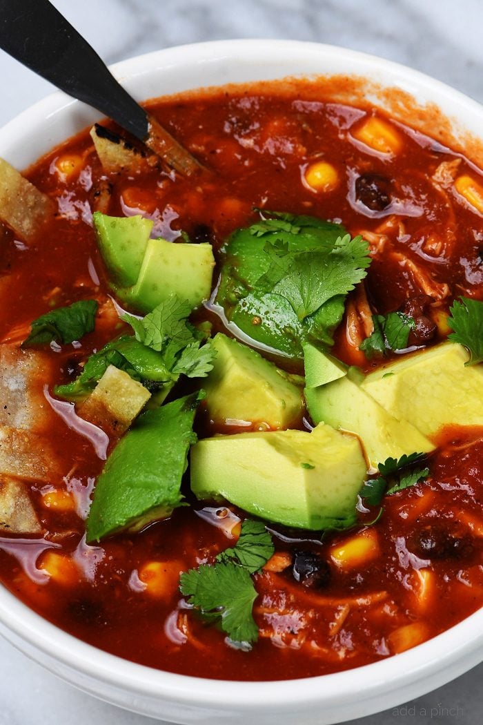 Chicken Tortilla Soup topped with chopped cilantro and avocado in a white bowl  // addapinch.com