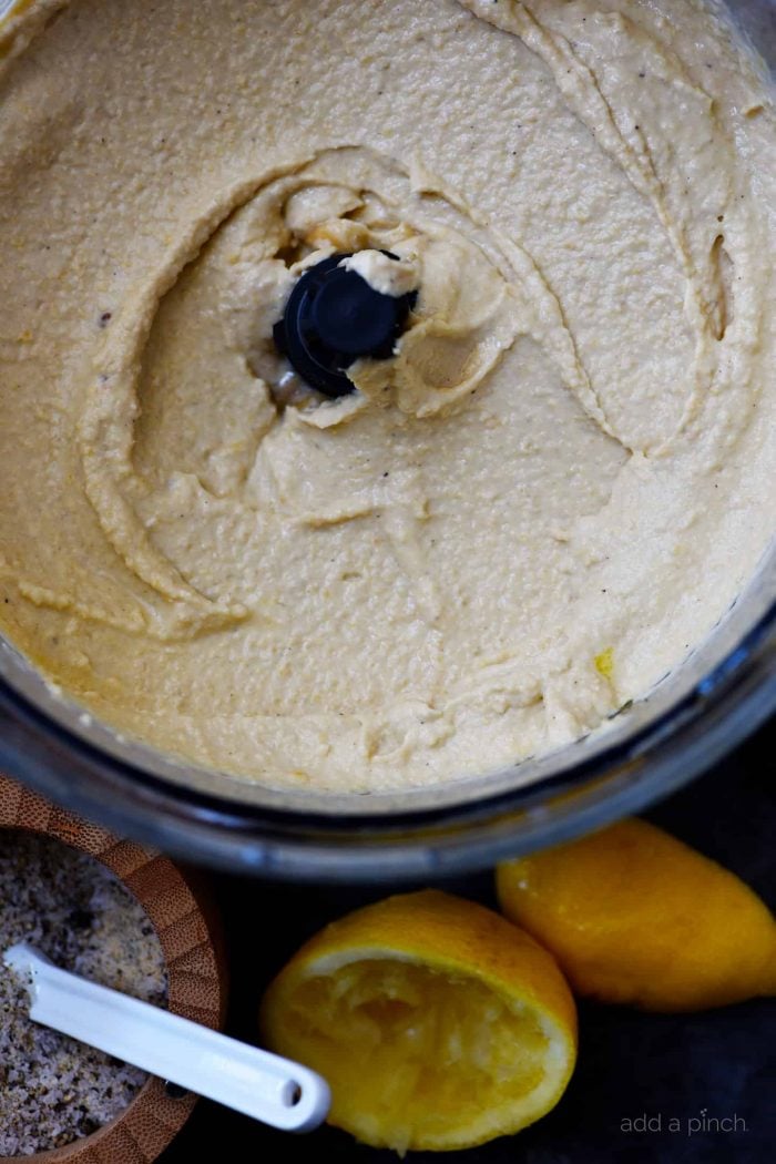 Creamy hummus after pulsing in a food processor, surrounded by lemon rinds and Stone House Seasoning and measuring spoon // addapinch.com