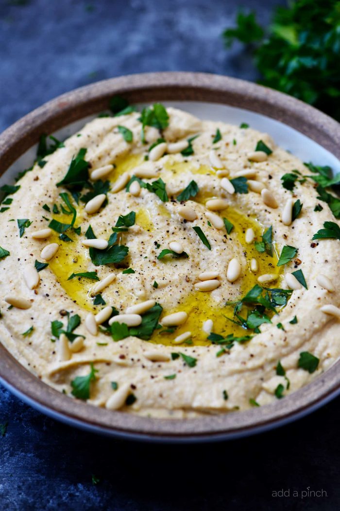 Side view of bowl of hummus topped with pine nuts and olive oil, as well as chopped parsley // addapinch.com