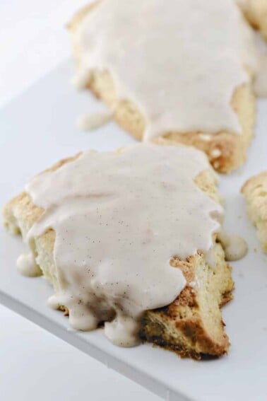 Scones topped with a vanilla bean glaze on a white platter.