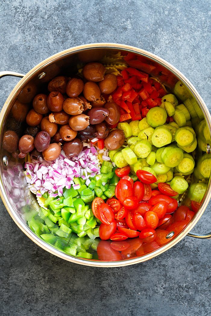 Large bowl filled with ingredients such as olives, cucumber, red onion, sliced cherry tomatoes, and red pepper. 