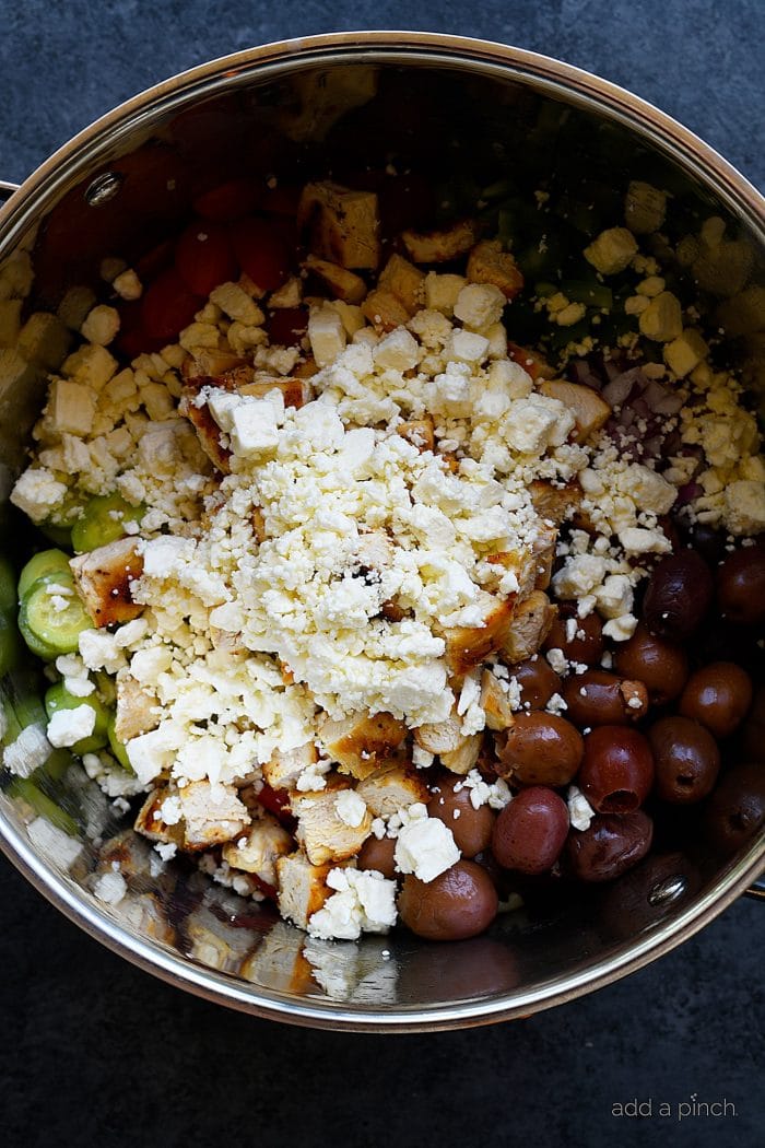Feta cheese tops grilled chicken, olives, vegetables in large bowl 