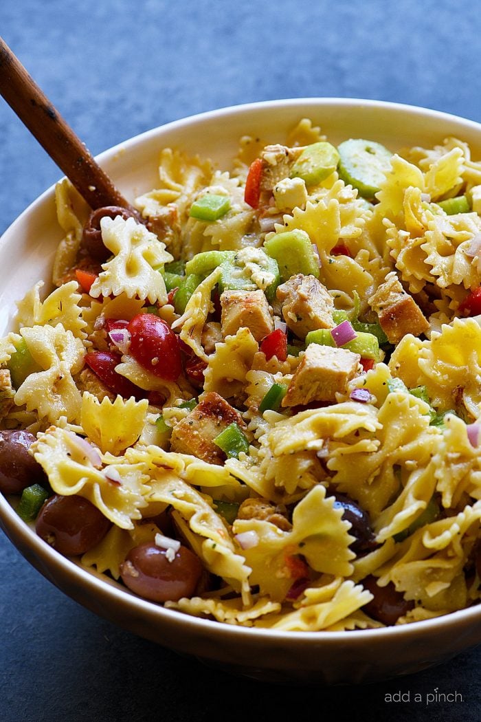 Pasta salad in large mixing bowl with wooden spoon