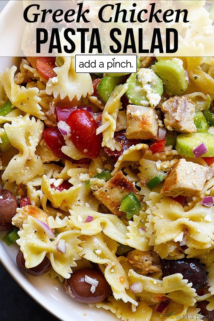 Closeup of Greek Chicken Pasta Salad with bowtie pasta, grilled chicken, olives, tomatoes, and more chopped vegetables - with text - addapinch.com