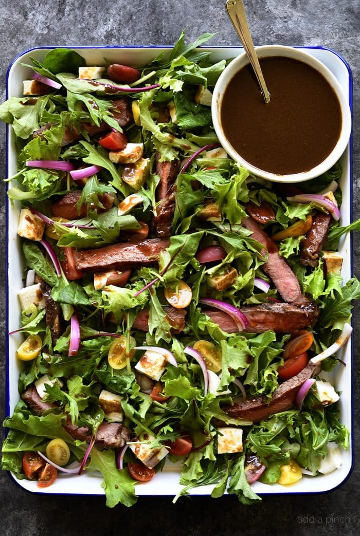 White enamel tray full of salad, steak strips and bowl of balsamic vinaigrette. // addapinch.com