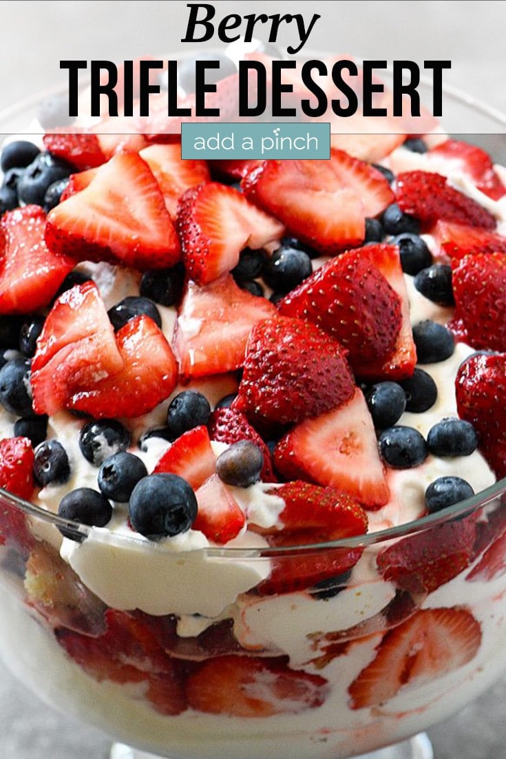 Strawberries and blueberries top a trifle dessert in glass bowl - with text - addapinch.com