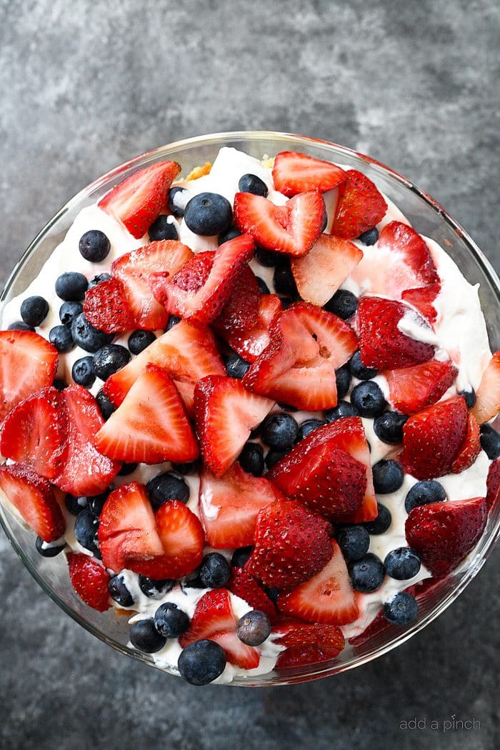 Glass trifle bowl with Berry Trifle, topped with juicy red strawberries and blueberries.
