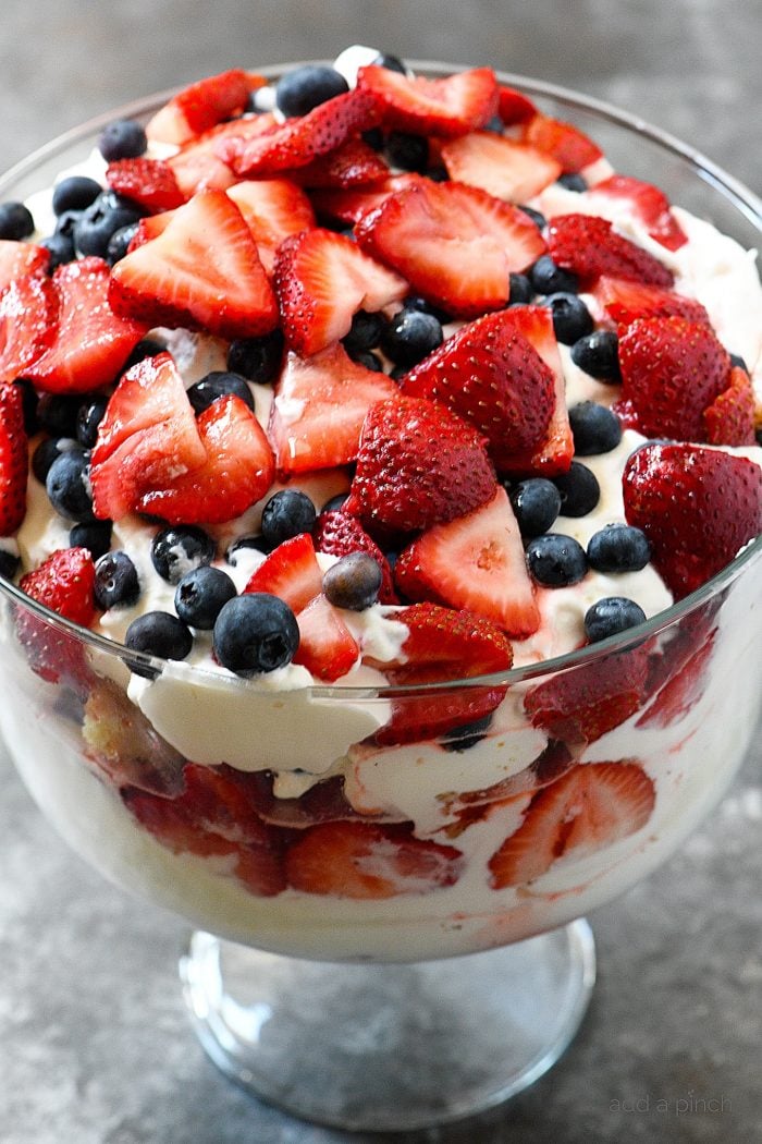 Layers of blueberries, strawberries, cake, whipped cream and pudding alternate in a glass trifle bowl. 