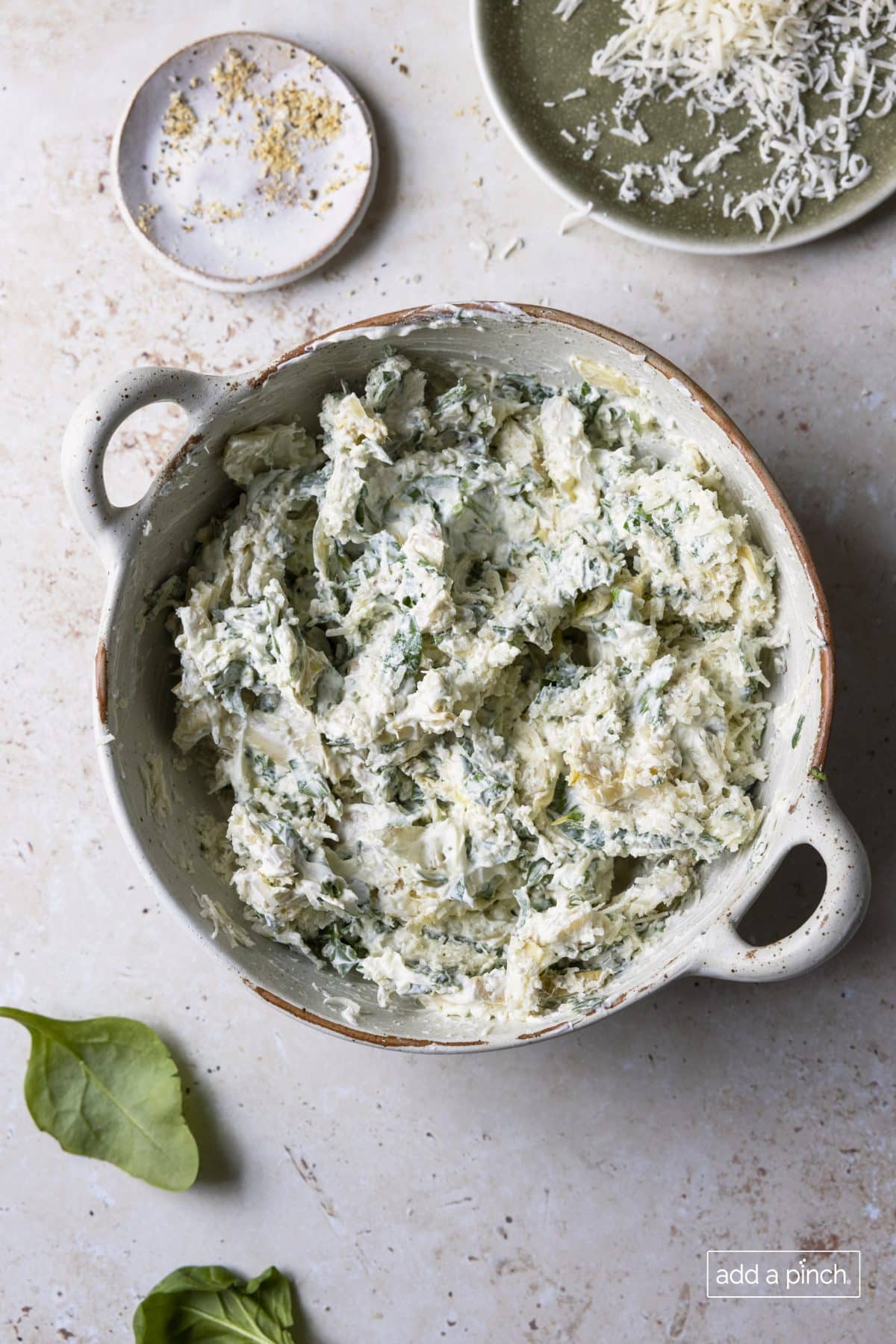 Photo of spinach artichoke dip combined together in a white baking dish ready to be topped with more cheese and baked.