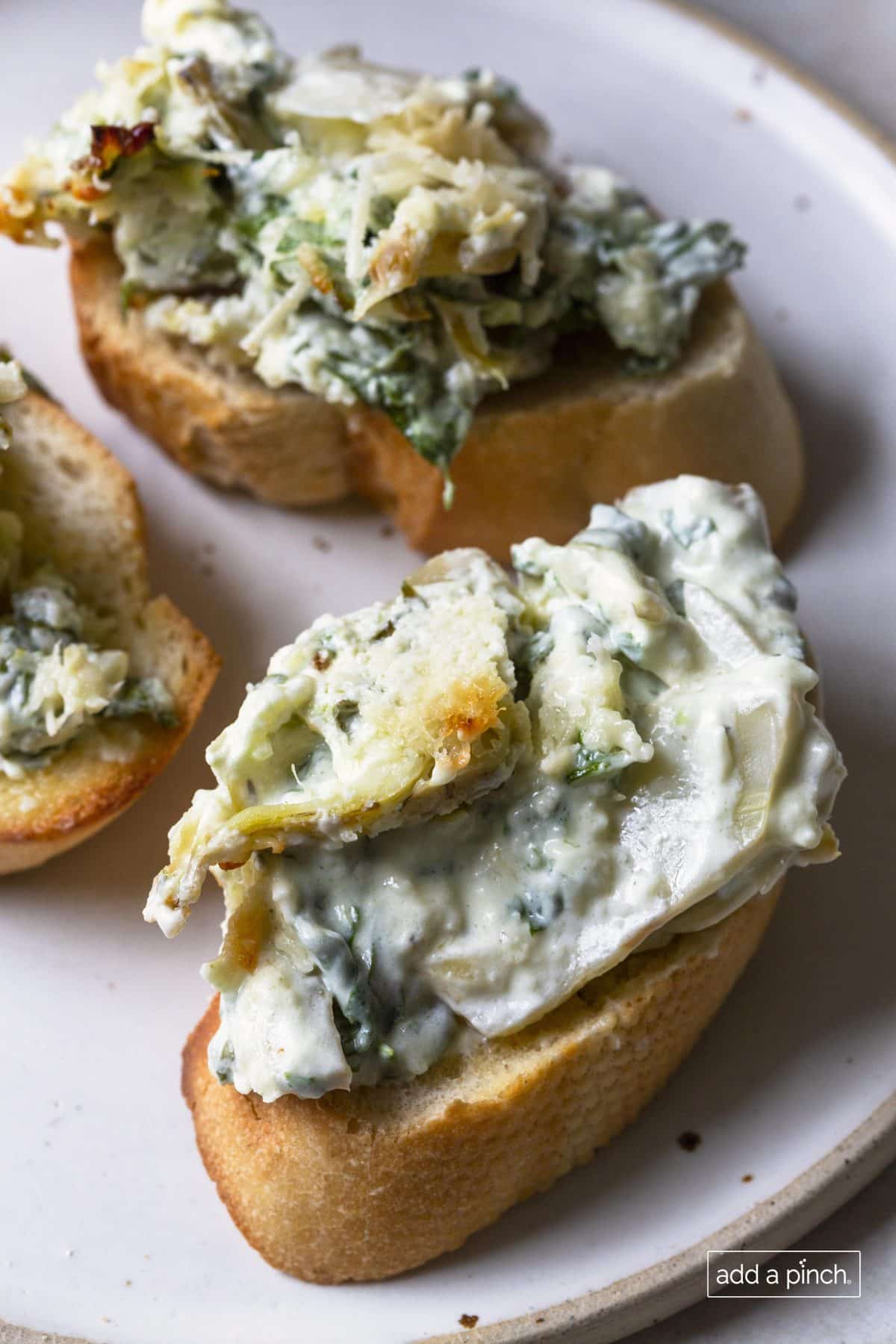 Photo of spinach artichoke dip on a toasted slice of baguette bread.
