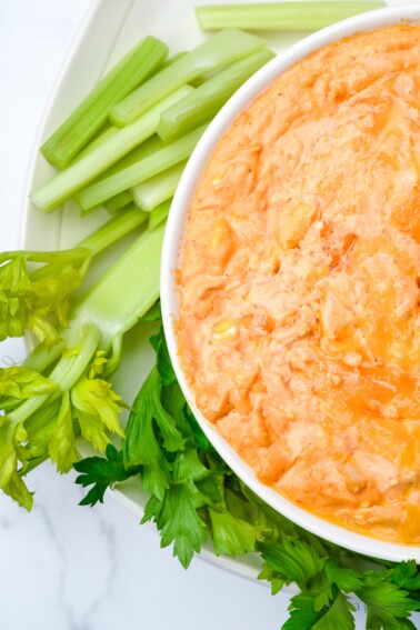 white bowl with buffalo chicken dip surrounded by celery on white background // addapinch.com