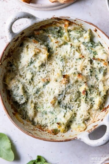 Photograph of baked spinach artichoke dip in a white serving dish.