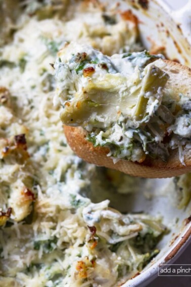Photo of spinach artichoke dip on a slice of toasted baguette.