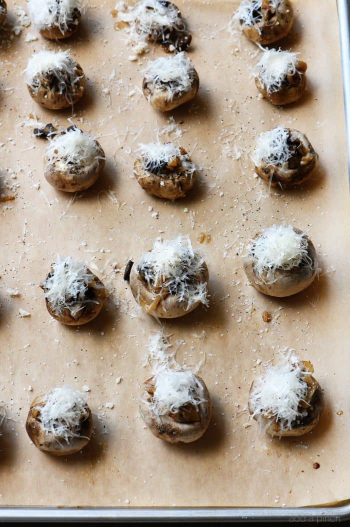 Parchment lined baking sheet holds rows of stuffed mushrooms topped with shredded cheese