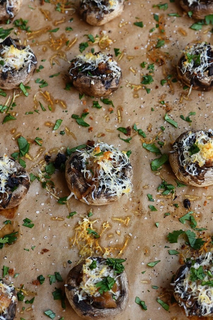 Overhead view of parchment lined baking sheet with stuffed mushrooms topped with cheese and parsley