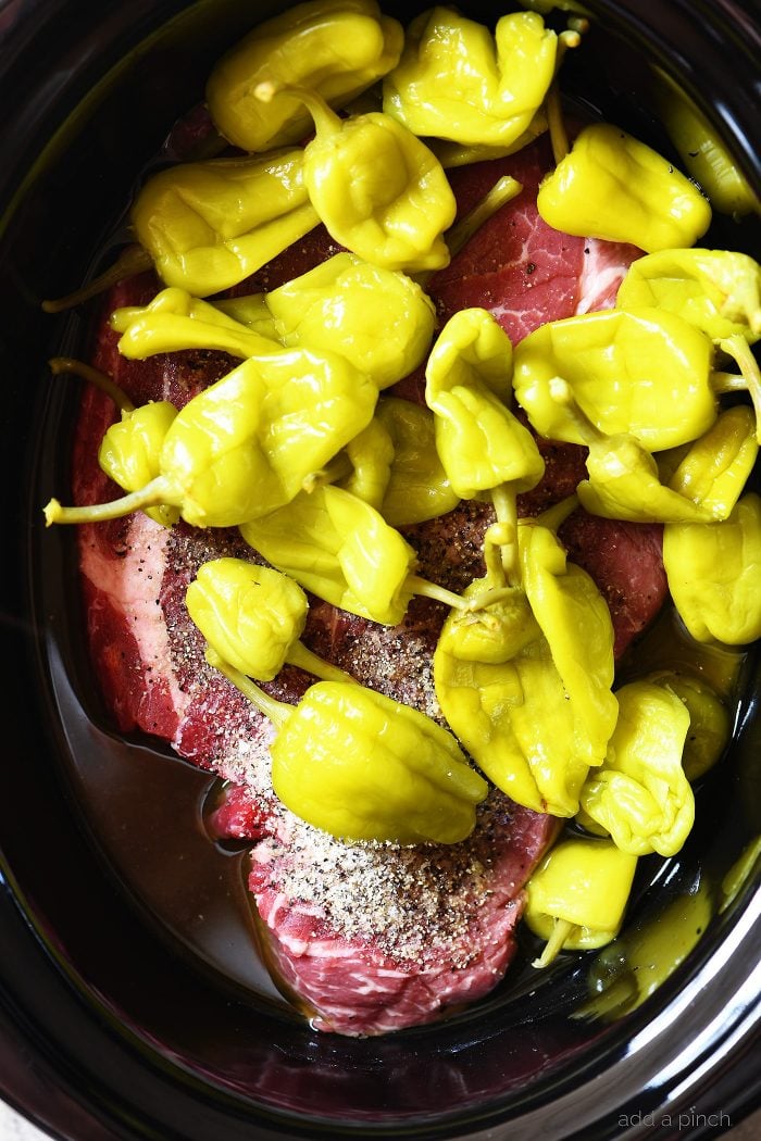 Slow Cooker has chuck roast sprinkled well with seasoning and topped with Pepperoncini peppers.   
