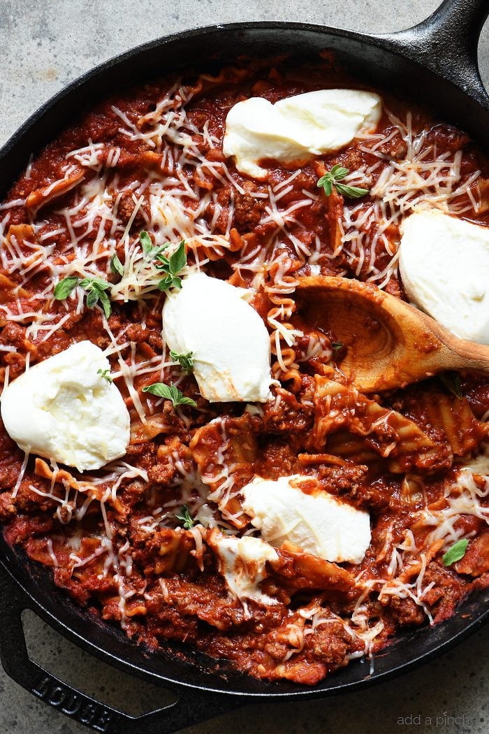 Iron skillet holds lasagna, meat sauce, ricotta cheese and parmesan as well as a wooden spoon. // addapinch.com
