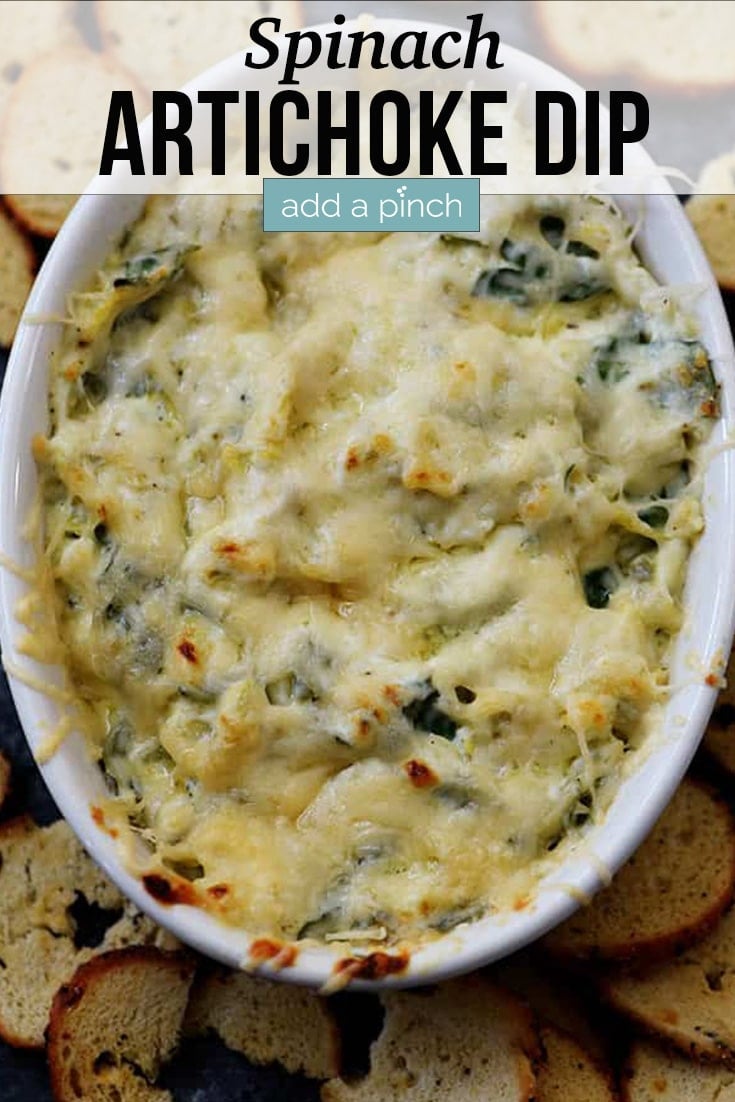 Cheesy Spinach Artichoke Dip in a white oval serving bowl, surrounded by bagel chips - with text - from addapinch.com