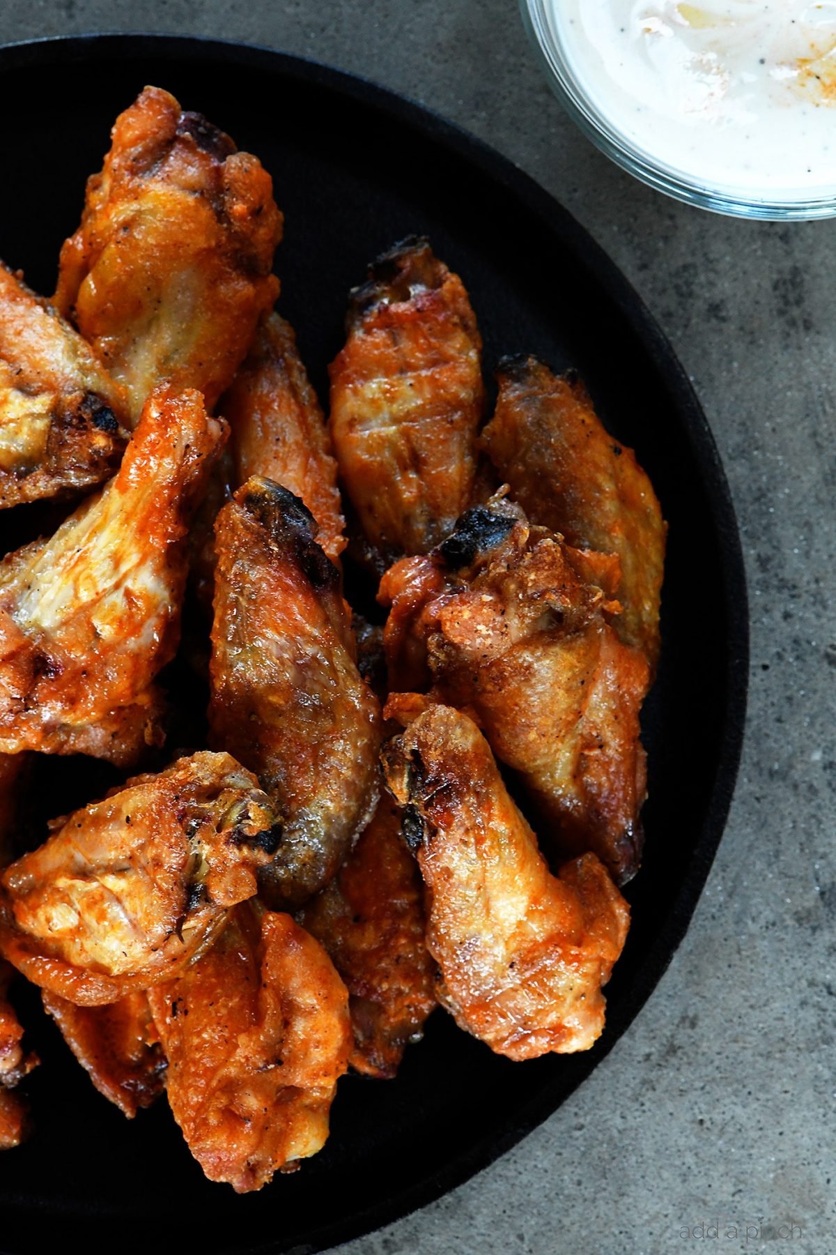 Chicken wings are baked until crispy and served on a black plate with ranch dressing for dipping.