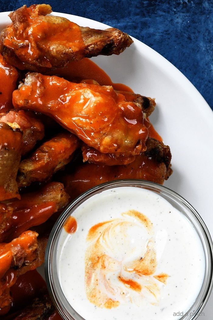 Chicken wings with buffalo sauce paired with ranch dressing in a glass cup all on a white plate.