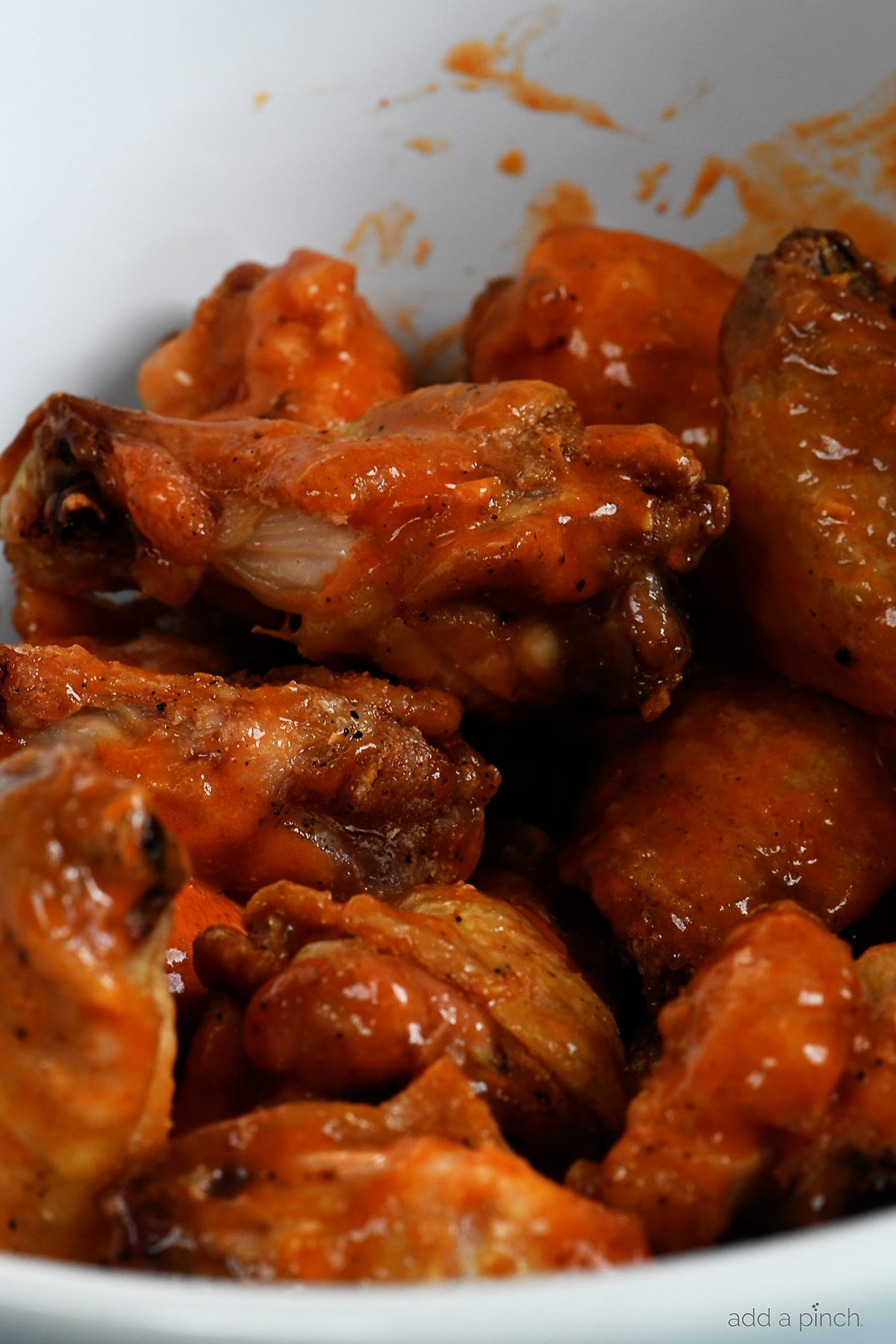 Chicken wings are tossed in homemade buffalo sauce in a white bowl.