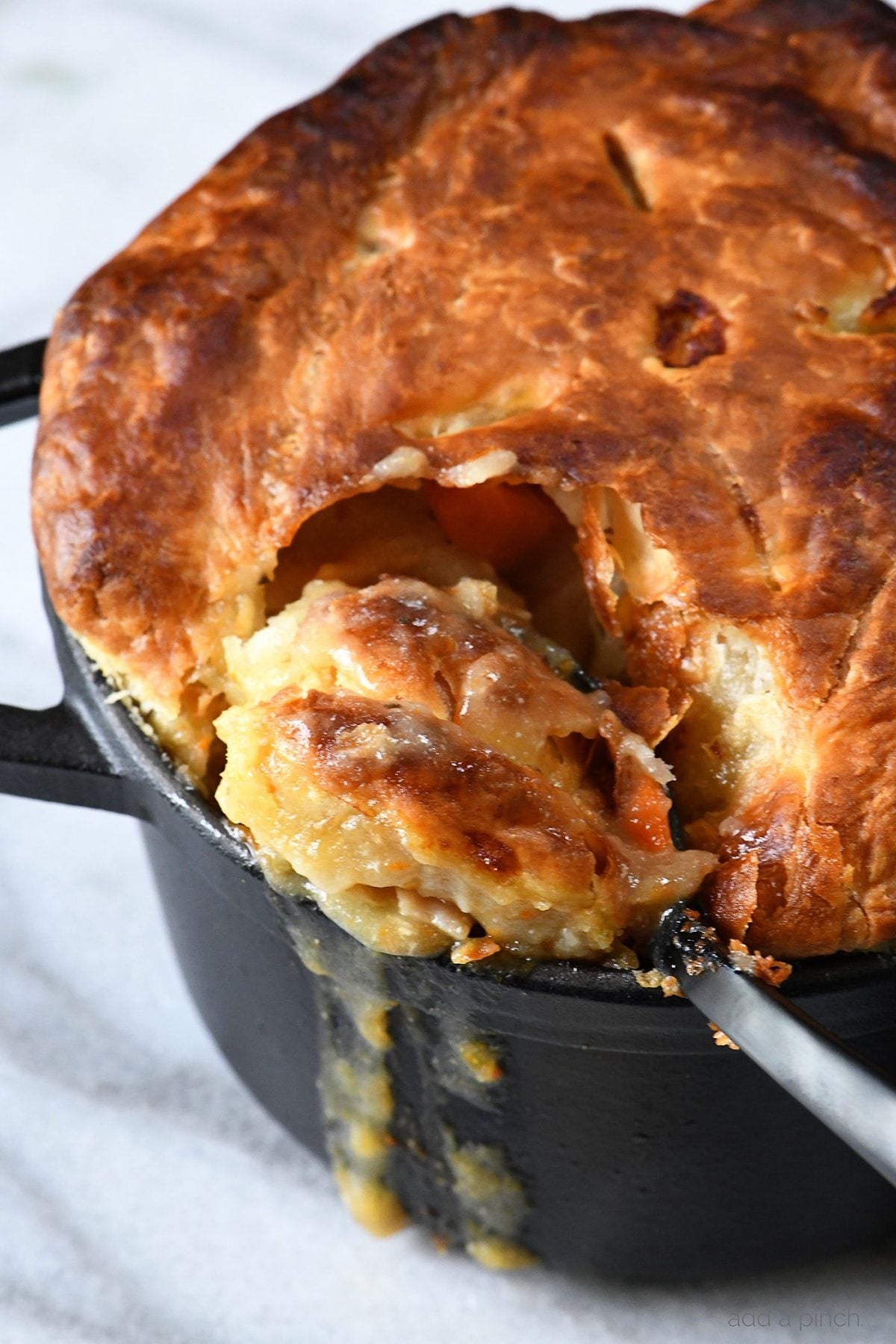 Black dutch oven holds a golden brown crust of a chicken pot pie being spooned out for serving.