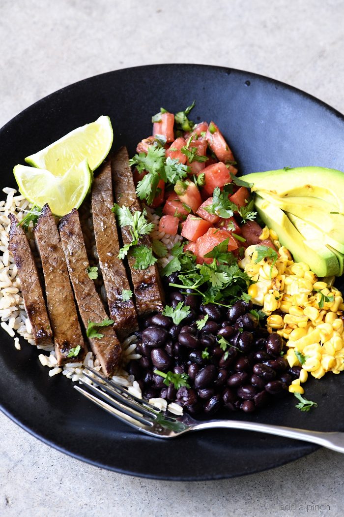 Serving bowl and fork with steak burrito bowl ingredients - steak, rice, beans, corn, pico, corn kernels and avocado slices 