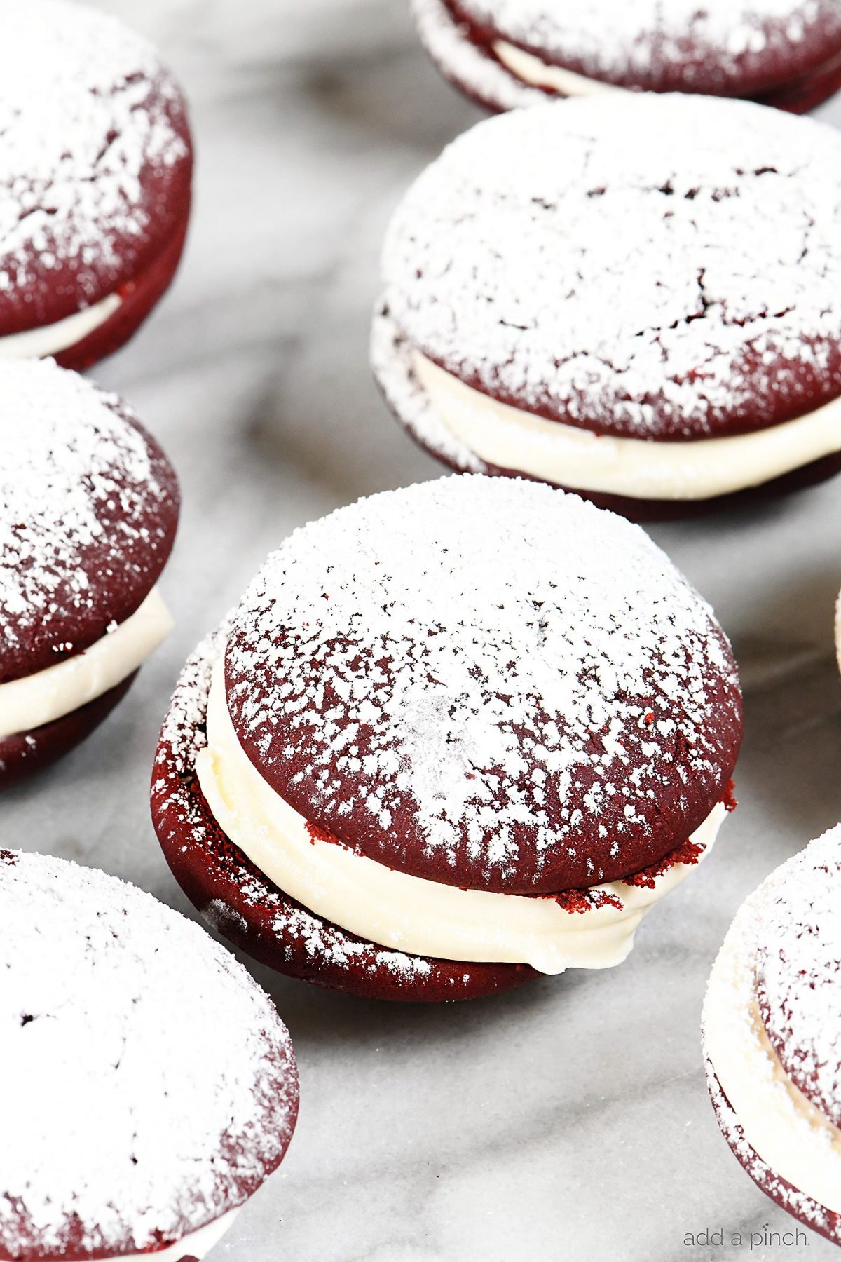 Red Velvet Cookies Recipe - These delicious cookies taste like your favorite red velvet cake in cookie form! Red Velvet cookies filled with cream cheese frosting and topped with a magical dusting of confectioner's sugar! // addapinch.com