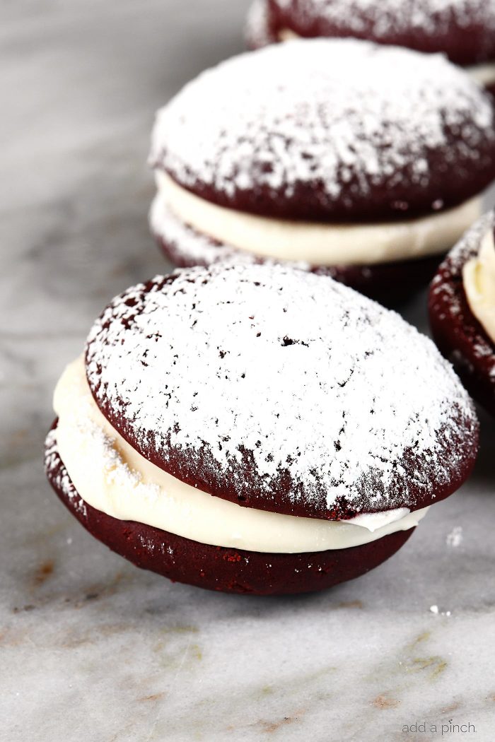 Red Velvet Cookies Recipe - These delicious cookies taste like your favorite red velvet cake in cookie form! Red Velvet cookies filled with cream cheese frosting and topped with a magical dusting of confectioner's sugar! // addapinch.com